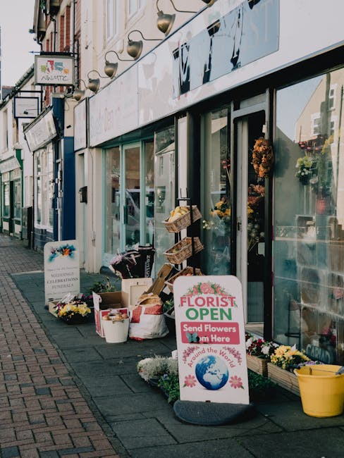 Outside Erith Florist, a flower shop on Erith High Street, displays a variety of fresh flowers and floral arrangements arranged in buckets and baskets on the pavement. The flowers include vibrant yell