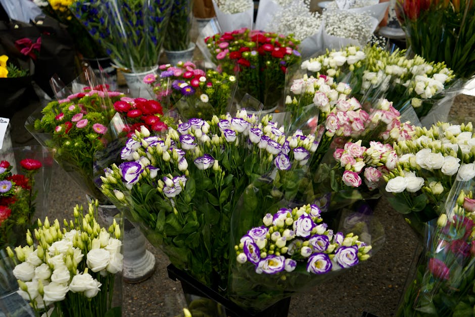 A collection of colorful flower bouquets arranged on a table, including purple and white lisianthus, pink and white roses, red and purple daisies, and white eustoma, all wrapped in clear plastic and s